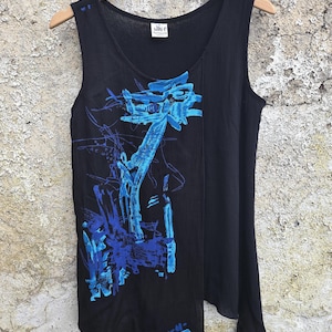 May include: A black sleeveless top with a round neckline and a textured fabric finish. The front features an abstract graphic print in shades of bright blue and dark blue. A white label with the text Anni E Particolari is sewn at the inner neck.