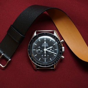 May include: A black-faced chronograph wristwatch with a silver band and a black leather strap. The watch face has a tachymeter scale and the words "Omega Speedmaster Professional" printed on it.