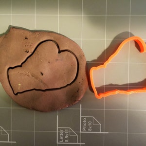 Puede incluir: Cortador de galletas de plástico naranja en forma de guante de boxeo. El cortador está al lado de una pieza de plastilina marrón con el contorno del cortador presionado en él.