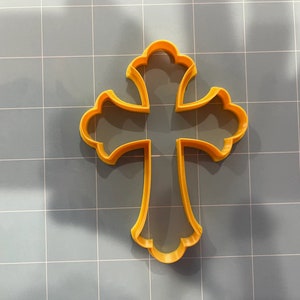 May include: A yellow plastic cookie cutter in the shape of a cross with ornate details.