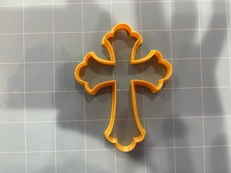 May include: A yellow plastic cookie cutter in the shape of a cross with ornate details.