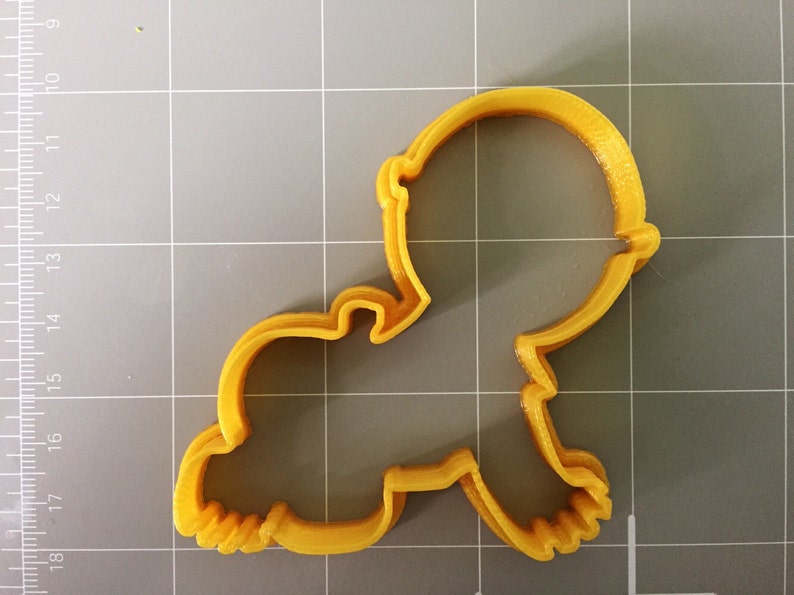 May include: A yellow plastic cookie cutter shaped like a baby. The cutter has a rounded head and a body with arms and legs.