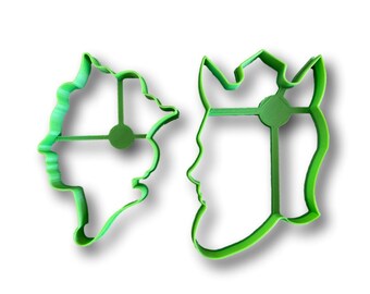 May include: Two green plastic cookie cutters shaped like faces. The cutter on the left is a woman's face and the cutter on the right is a man's face.