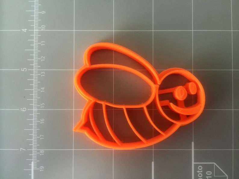 May include: Orange plastic cookie cutter shaped like a cartoon bee with a smiling face and striped body.