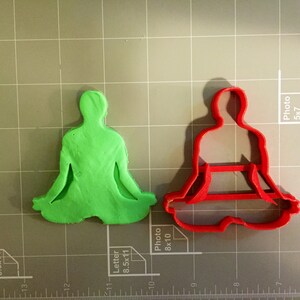 May include: Two cookie cutters, one green and one red, shaped like a person sitting in a yoga pose.