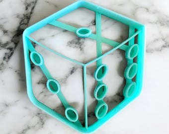 Puede incluir: Un cortador de galletas de plástico azul turquesa con forma de dado de seis caras con un patrón de puntos en relieve en cada cara.