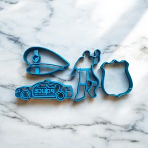 Pode incluir: Um conjunto de cinco cortadores de biscoitos de plástico azul em forma de policial, carro de polícia, chapéu de polícia, distintivo e policial. O carro de polícia tem a palavra "POLICE" escrita no lado.
