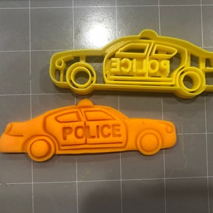 Pode incluir: Dois cortadores de biscoitos de plástico amarelo em forma de carro de polícia. O cortador superior é um design de corte e o cortador inferior é um design sólido. Ambos os cortadores têm a palavra "POLICE" impressa na lateral.