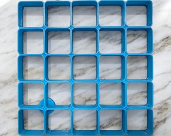 May include: A blue plastic grid with 36 square compartments. One compartment is missing.