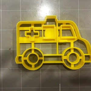 May include: Yellow plastic cookie cutter shaped like an ambulance. The cutter has a cross on the side and a window on the front.