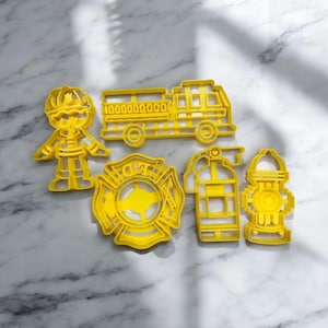 Pode incluir: Conjunto de cinco cortadores de biscoitos de plástico amarelo em forma de bombeiro, caminhão de bombeiros, hidrante, extintor e um distintivo do departamento de bombeiros. O distintivo tem as letras "FD" e as palavras "Fire Department".