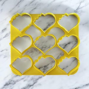 Peut inclure: Emporte-pièce en plastique jaune avec neuf découpes en forme de cœur.