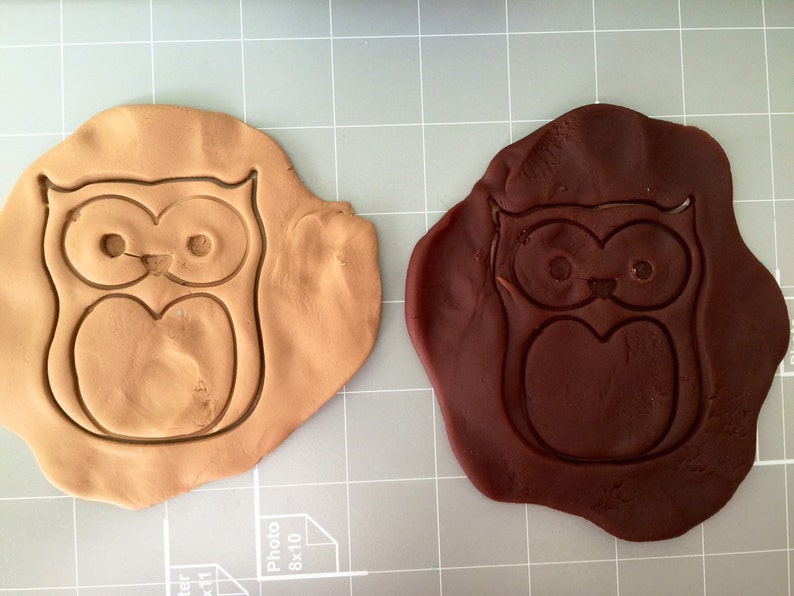 May include: Two owl-shaped cookie cutters, one brown and one dark brown, on a gray grid surface.