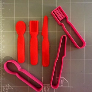 Puede incluir: Cinco cortadores de galletas de plástico rojo y rosa con forma de cuchara, tenedor, cuchillo y dos estilos diferentes de cucharas.
