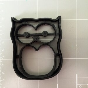 May include: Black plastic owl cookie cutter. The cutter has a detailed design with eyes, beak, and body.