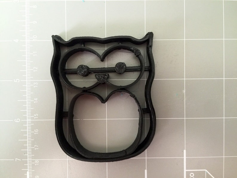 May include: Black plastic owl cookie cutter. The cutter has a detailed design with eyes, beak, and body.