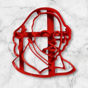 May include: Red plastic cookie cutter shaped like a profile of William Shakespeare. The cutter is designed with a detailed outline of his face, hair, and collar.