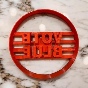 May include: Red plastic cookie cutter in the shape of a circle with the words "VOTE BLUE" printed inside.