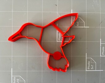 Puede incluir: Un cortador de galletas de plástico rojo en forma de colibrí. El cortador tiene la forma de un colibrí en vuelo con las alas extendidas.