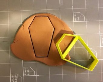 May include: A yellow plastic cookie cutter shaped like a coffin, on top of a brown fondant base.