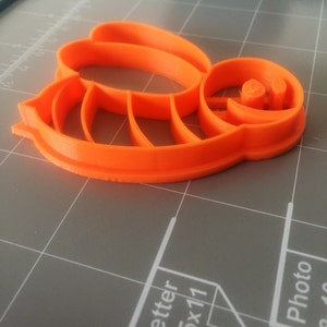 May include: Orange plastic bee-shaped cookie cutter. The cutter has a detailed design with wings and a face.