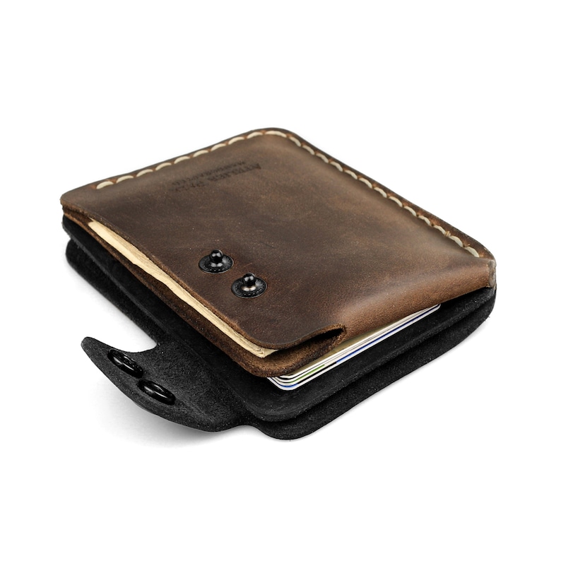 May include: A brown leather wallet with a black interior and snap closure. The wallet is filled with cards and has white stitching along the edges. The text "ATELIER VALE" is visible on the top.