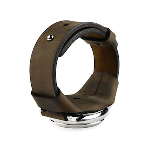 Może przedstawiać: Bransoleta ze skóry w kolorze brązowym ze srebrnym metalowym akcentem. Bransoleta ma szeroki pasek i prosty, nowoczesny design. Skóra wydaje się postarzana, nadając jej wygląd vintage.