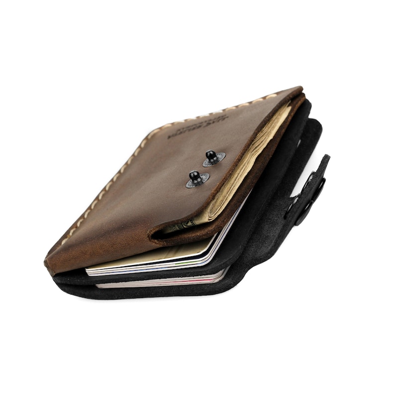 May include: A brown leather wallet with a bi-fold design. The wallet is open, revealing multiple compartments for cards and cash. The leather has a distressed appearance, and the stitching is visible. Two metal snaps secure the wallet.