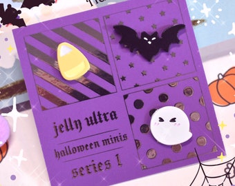 May include: A purple card with four Halloween-themed mini pins: a candy corn, a bat, and a ghost. The card has the text "Happy Halloween" and "Jelly Ultra Halloween Minis Series 1".