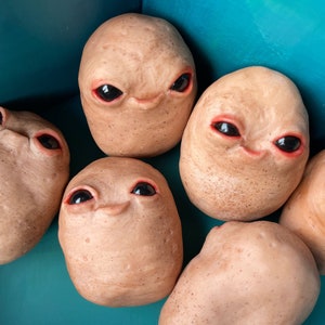 Puede incluir: Seis pequeñas esculturas de cerámica marrón con rasgos humanos, incluidos ojos, narices y bocas. Las esculturas están dispuestas en círculo sobre una superficie azul.