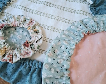 May include: Three circular fabric bowl covers with elasticized edges. One large cover features a white center with green leaf patterns and a blue floral border. A smaller cover has a floral print, and another has a light green daisy print on pink.