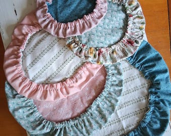 May include: A collection of four circular fabric bowl covers with elasticized edges. The covers feature various patterns including solid dusty pink, teal with small white dots, and a light green floral print with white and yellow flowers.