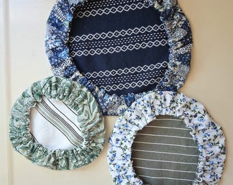 May include: Three circular fabric bowl covers with elasticized edges. The largest cover features a dark blue center with white geometric patterns and a blue floral border. Two smaller covers feature green floral and blue floral patterns respectively.