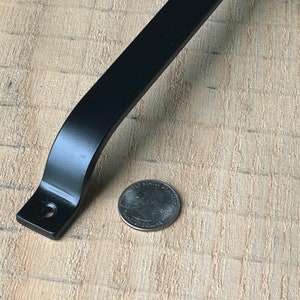 May include: Black metal door handle with rounded edges and two screw holes. The handle is approximately 6 inches long.