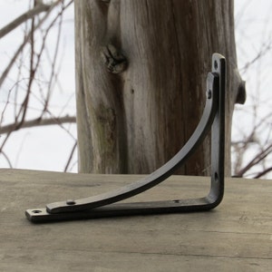 May include: A black metal shelf bracket with a curved design. The bracket is made of sturdy metal and has a rustic finish.