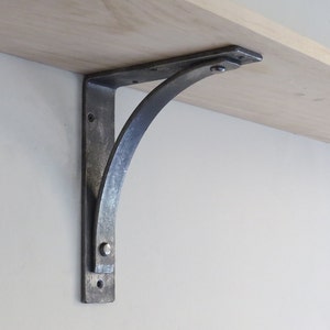 May include: A silver metal shelf bracket with a curved design. The bracket is attached to a wooden shelf.