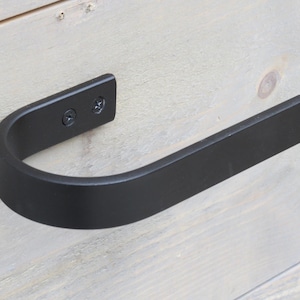 May include: Black metal towel bar with a curved design. The bar is mounted to a light wood surface with two screws.