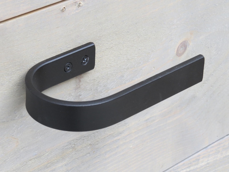 May include: Black metal towel bar with a curved design. The bar is mounted to a light wood surface with two screws.