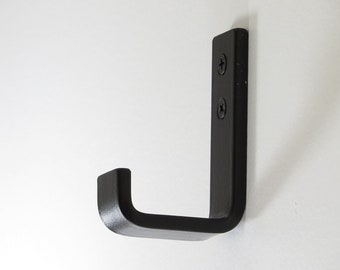May include: Black metal hook with a rounded edge. The hook is mounted to a white wall.