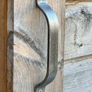 May include: A silver metal door handle with a curved design and two screws. The handle is mounted on a wooden door.