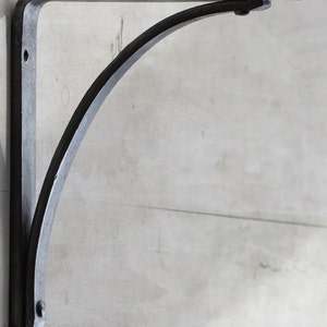 May include: A black metal shelf bracket with a curved design. The bracket is mounted to a wall.