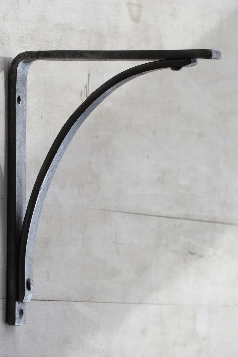 May include: A black metal shelf bracket with a curved design. The bracket is mounted to a wall.