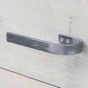 May include: A silver metal towel bar with a curved design. The bar is mounted to a light wood surface.