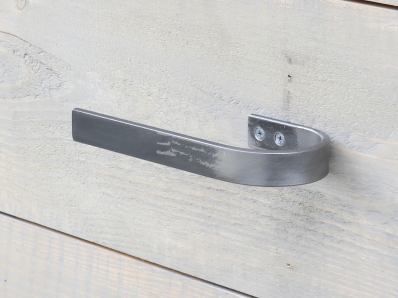 May include: A silver metal towel bar with a curved design. The bar is mounted to a light wood surface.