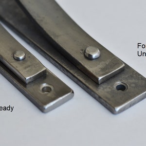 May include: Two metal strips, one with a rough, unfinished surface and the other with a smooth, paint-ready surface. Both strips have a rounded edge and a small hole at one end. The text "Forge-fired Unfinished" is above the rough strip and "Paint-ready" is below the smooth strip.