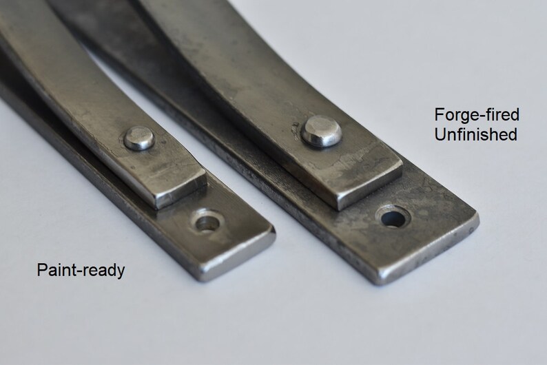 May include: Two metal strips, one with a rough, unfinished surface and the other with a smooth, paint-ready surface. Both strips have a rounded edge and a small hole at one end. The text "Forge-fired Unfinished" is above the rough strip and "Paint-ready" is below the smooth strip.