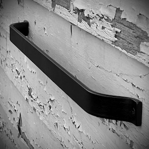 May include: Black metal towel bar mounted on a white wall with peeling paint.