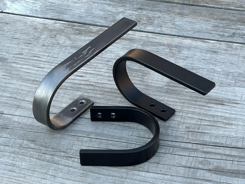 May include: Two metal shelf brackets, one in a brushed silver finish and one in black. Both brackets have a curved shape and are designed to be mounted to a wall.