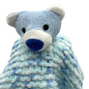 May include: A blue plush bear head with a white muzzle and ears, and black eyes. The bear is attached to a soft, chunky knit blanket in shades of blue and white. A comforting baby item.