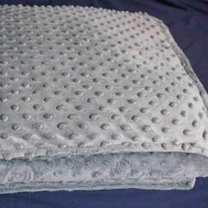 May include: A gray weighted blanket with a textured surface. The blanket is folded in half and has a soft, plush feel.